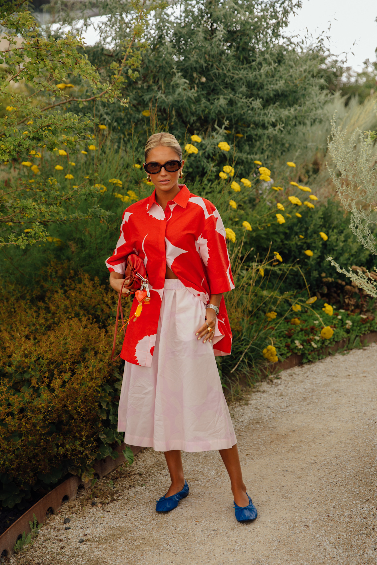A copenhagen spring 2025 fashion week attendee wears a printed button down, pink skirt, and blue flats