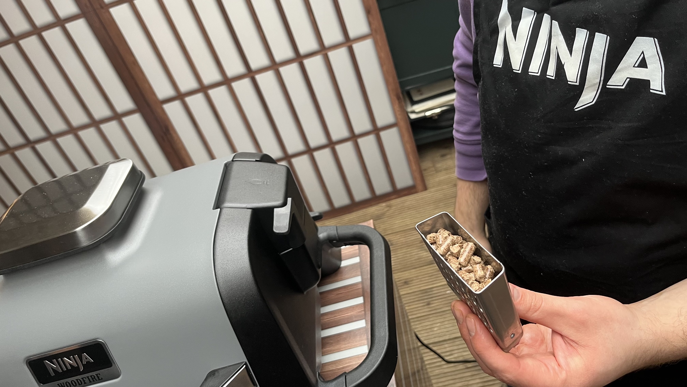 ninja woodfire grill with pellets tray held in the hand of a demonstrator