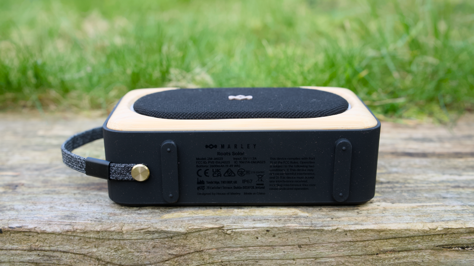 House of Marley Roots Solar Bluetooth speaker outdoors in a garden, on a wooden bench.