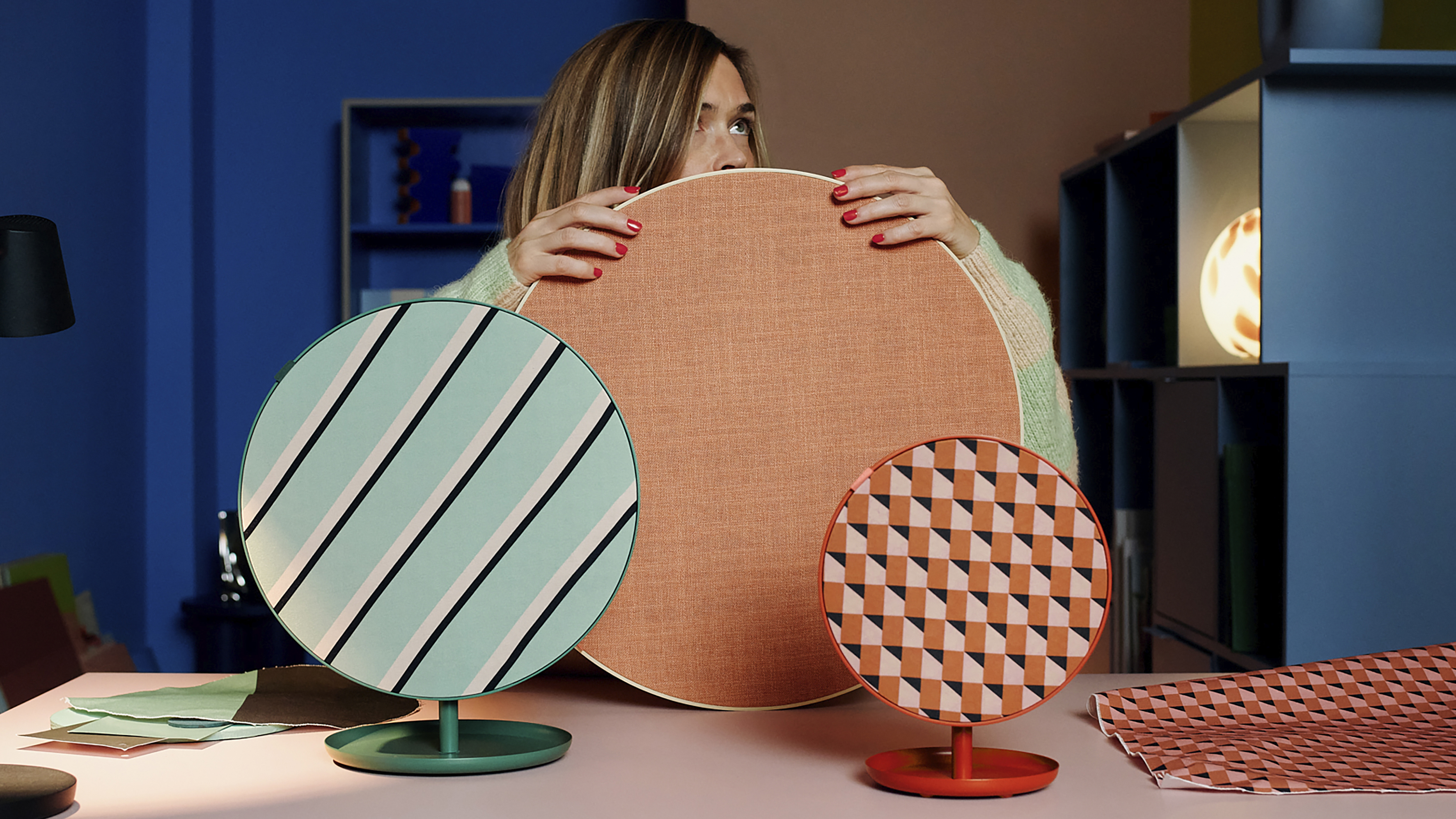 Three IKEA Bluetooth speakers on a table with a person holding one of them