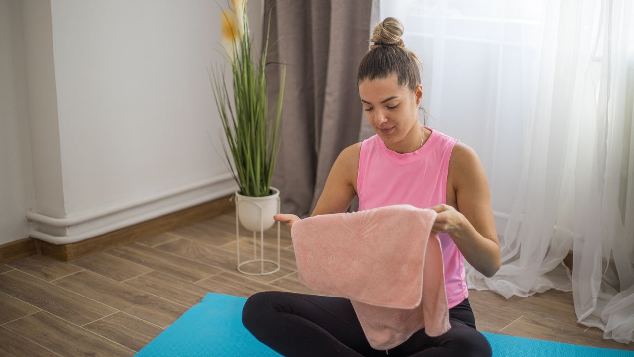 Woman in sportswear sitting cross-legged on exercise mat holding towel