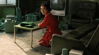 Gemma sits writing thank you notes in a festive robe in a 1950s style room on the testing floor in Severance Season 2.