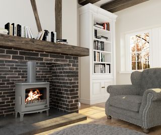 grey freestanding log burner in brick fireplace with wooden mantle and cosy grey armchair in front of fire