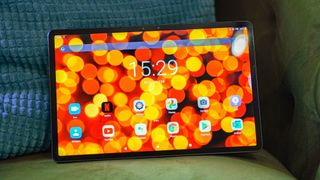 A Lenovo Tab P11 Pro with the screen on, resting against a cushion