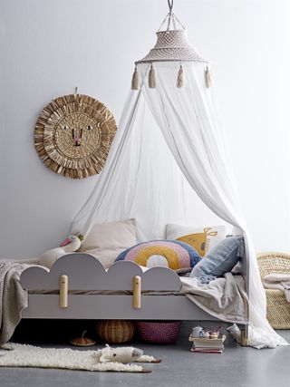 A girls bedroom with a canopy bed with cotton drapes and lots of soft cushions