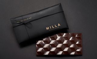 Milla Chocolates hazelnut praline bar (one gift wrapped and one open bar) photographed against a black background