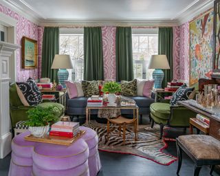 A living room with pink and white wallpaper, green curtains, artwork and an eclectic mix of multicolored wallpaper in a maximalist style