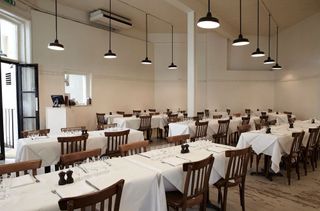 Interior view of St. John's restaurant, Spitalfields with tables covered in white cloth, brown chairs and black pendant lights