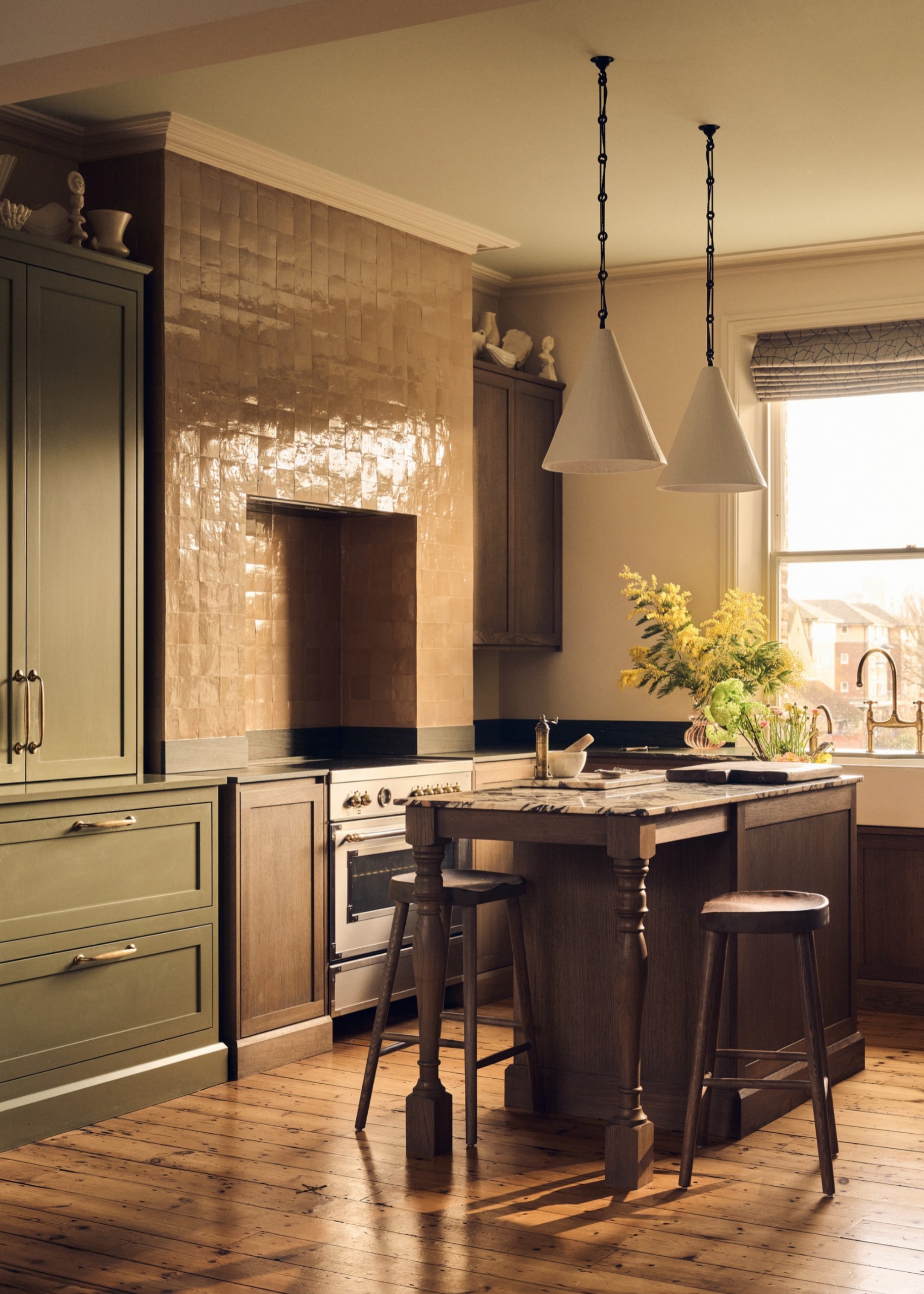 A kitchen with green cabinets, dark wood island and two cone-shaped pendants hanging over the island