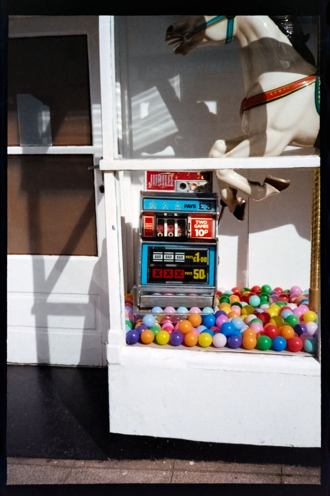 Cropped scan of an amusement arcade display featuring a vintage slot machine surrounded by colorful plastic balls beneath a carousel horse.