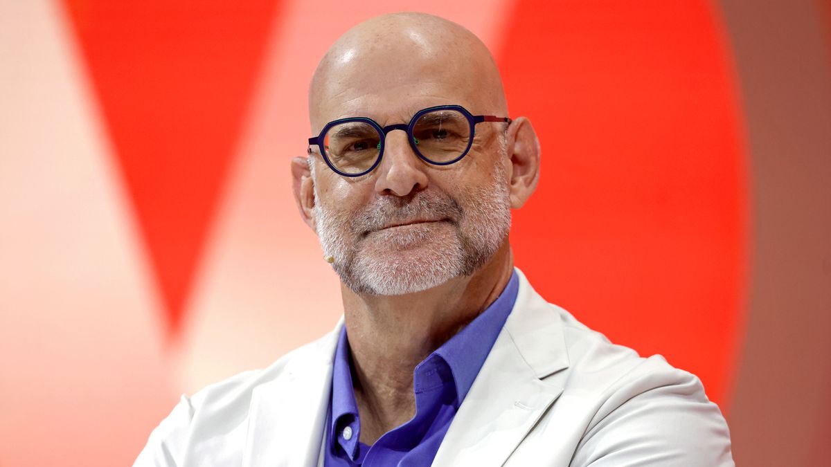 Harlan Coben weaing a light jacket and sitting in front of a red background and smiling 