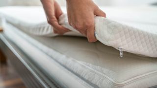 A cooling mattress topper is placed on top of a white hybrid mattress