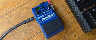 A DigiTech JamMan Solo HD looper pedal on a wooden floor, next to a pedalboard