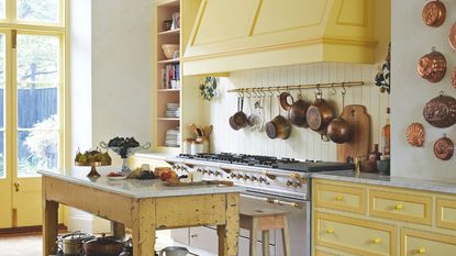 Yellow kitchen styled with vintage pots, accessories and copper jelly moulds hanging on the wall