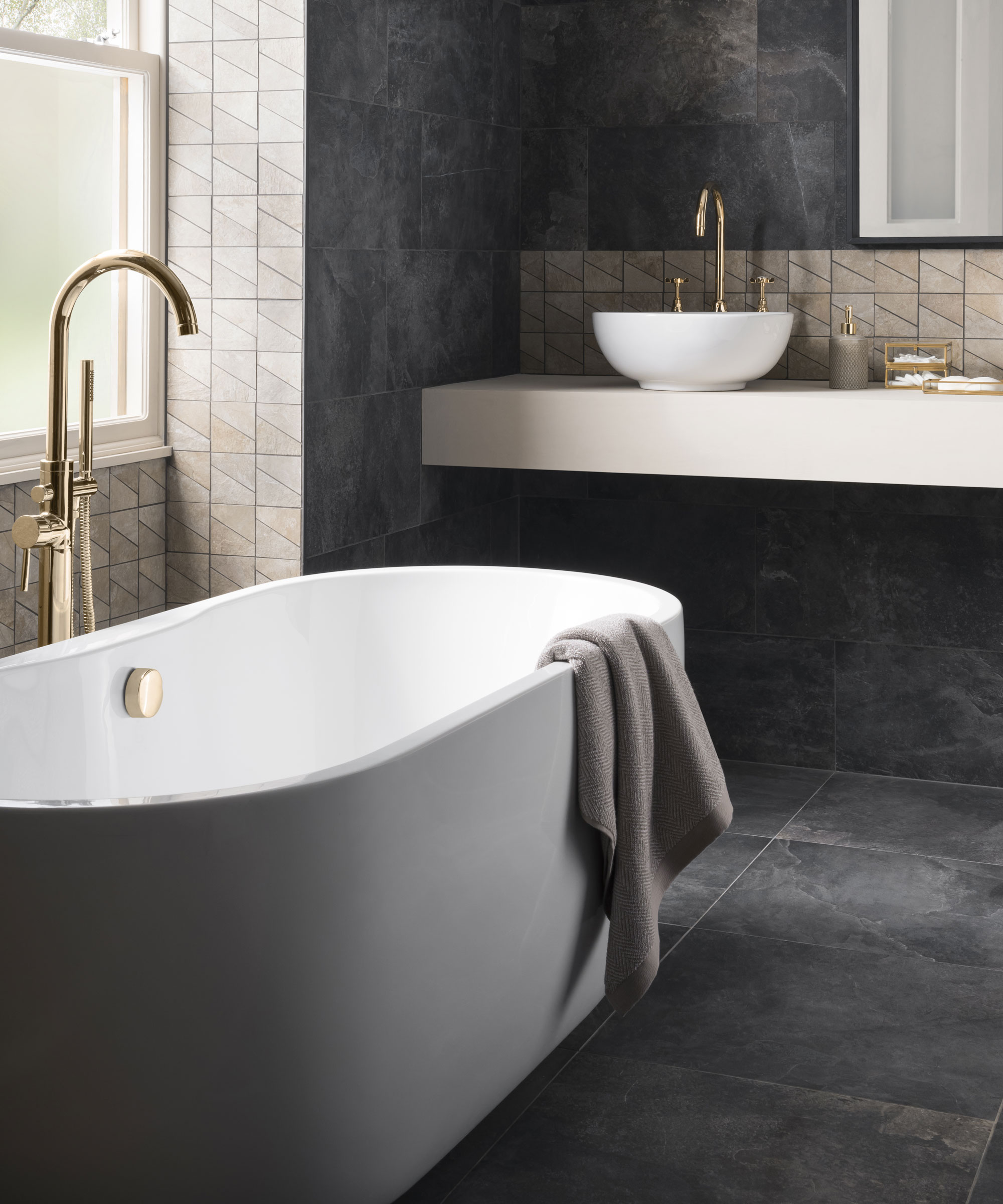 An example of small bathroom tile ideas showing a gray free-standing bath in front of large, dark gray floor and wall tiles