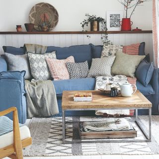 A living room with a cushiony blue linen corner sofa adorned with contrasting scatter cushions