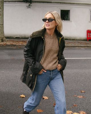 Fashion influencer Lucy Williams in London wearing a chic fall outfit with a Barbour barn coat styled with jeans, black loafers, white socks, and a crewneck knit sweater.