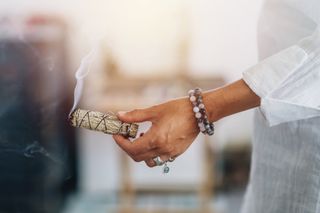 Midsection Of Sage Holding Feather With Smudge Stick While Standing Indoors