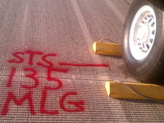 Workers measured and marked in bright red the letters "MLG" at the spot where space shuttle Atlantis' main landing gear came to rest after the vehicle's final return from space.