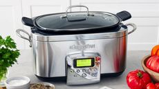 A silver GreenPan Elite 6 Quart Slow Cooker next to herbs, spices and tomatoes