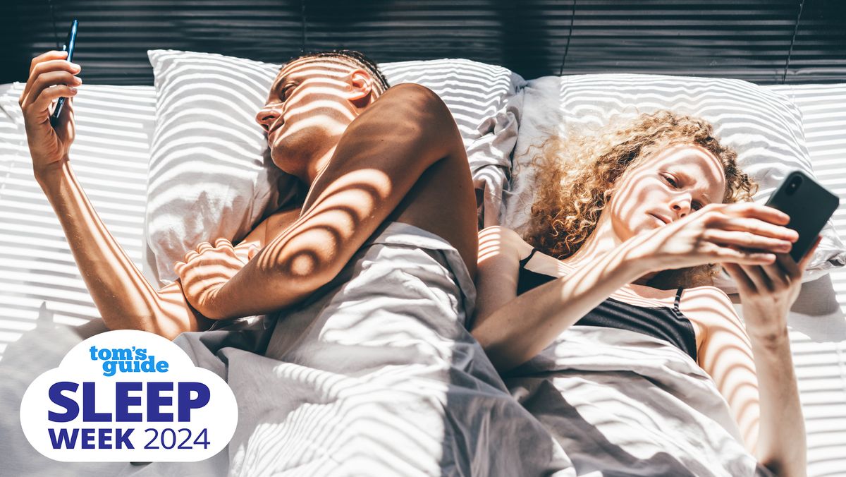 A young couple scroll on their phones in bed, which can contribute to insomnia 