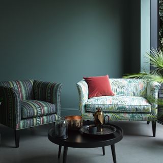 a green living room with two different green pattern sofas with a black coffee table