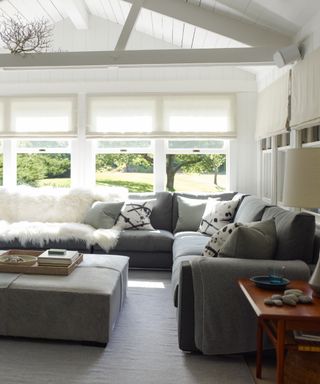 living room/sunroom with grey sectional, view outside, footstool blinds