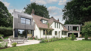 Exterior of a cream house with green window frames, with an extension on either side and a patio and lawn in front