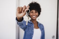 Happy woman showing house keys standing in front of door