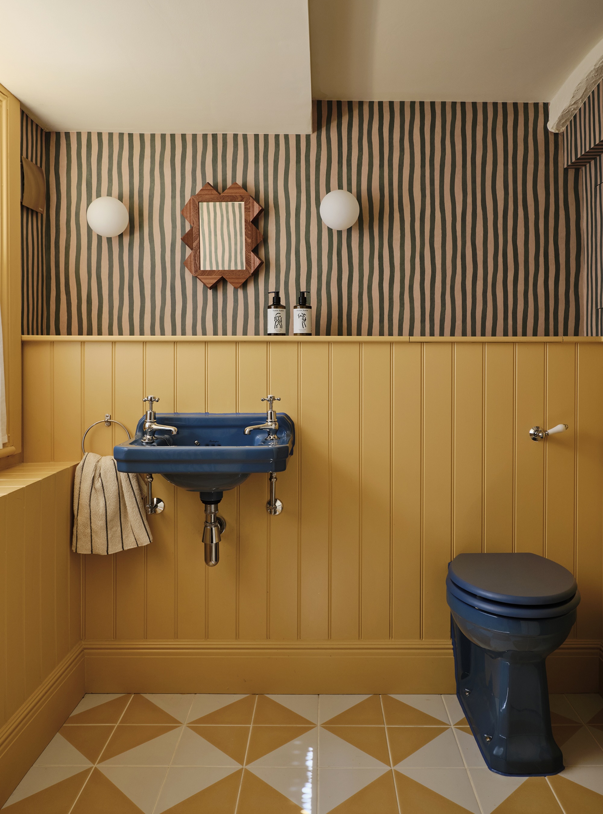 Ochre yellow bathroom with inky blue sink and toilet and striped wallpaper