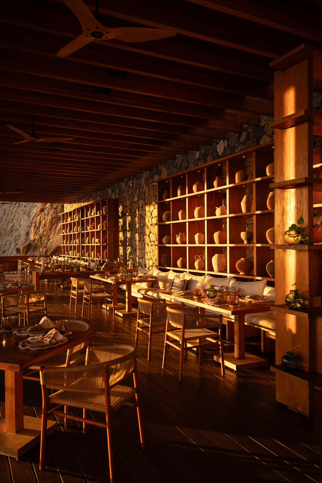 Four Seasons Tamarindo's restaurant Sal at golden hour, next to the ocean and lit in an orangey hue. Featuring wooden interiors and pottery accents.