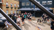 A bike shop courtyard is shown with many cyclists standing outside of it