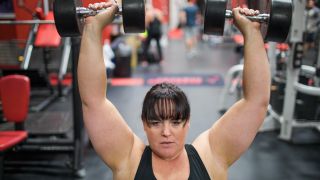 Woman performs dumbbell shoulder press in gym