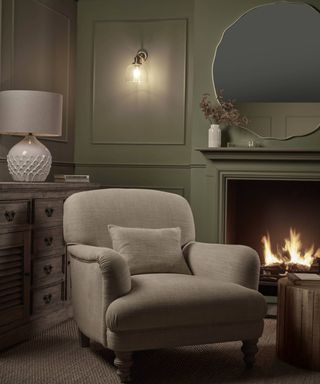 cosy green living room with armchair, lit fire and glass wall light