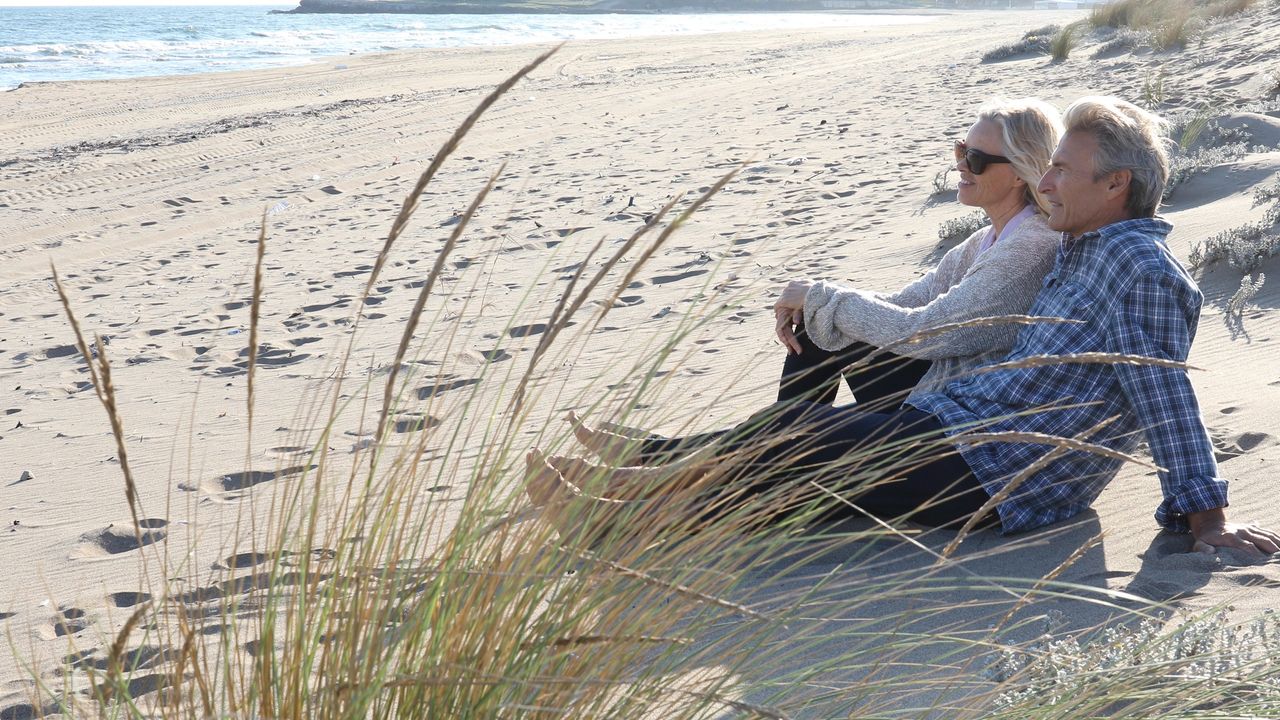 A couple who embraced early retirement sit on the beach together.