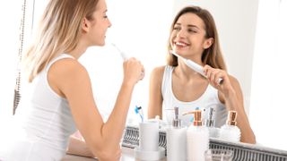 Woman brushing her teeth with electric toothbrush while looking in mirror