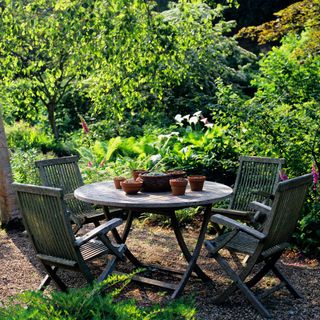 wooden garden table and chairs in a shaded woodland area of garden