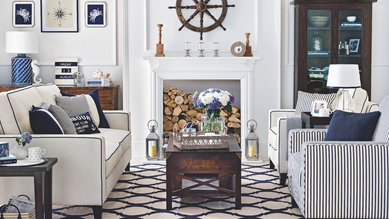 vintage living room with nautical theme, blue and white colours, boat wheel, nautical ornaments, stripe armchairs, white and blue sofa, blue and white cushions, blue and white rug, wood coffee table, logs in fireplace, lanterns, storage unit, sideboard