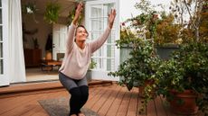 Woman practicing yoga on wooden decking outdoors in front of French doors