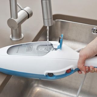 Close up of a Black & Decker steam mop being filled with water from a kitchen tap.