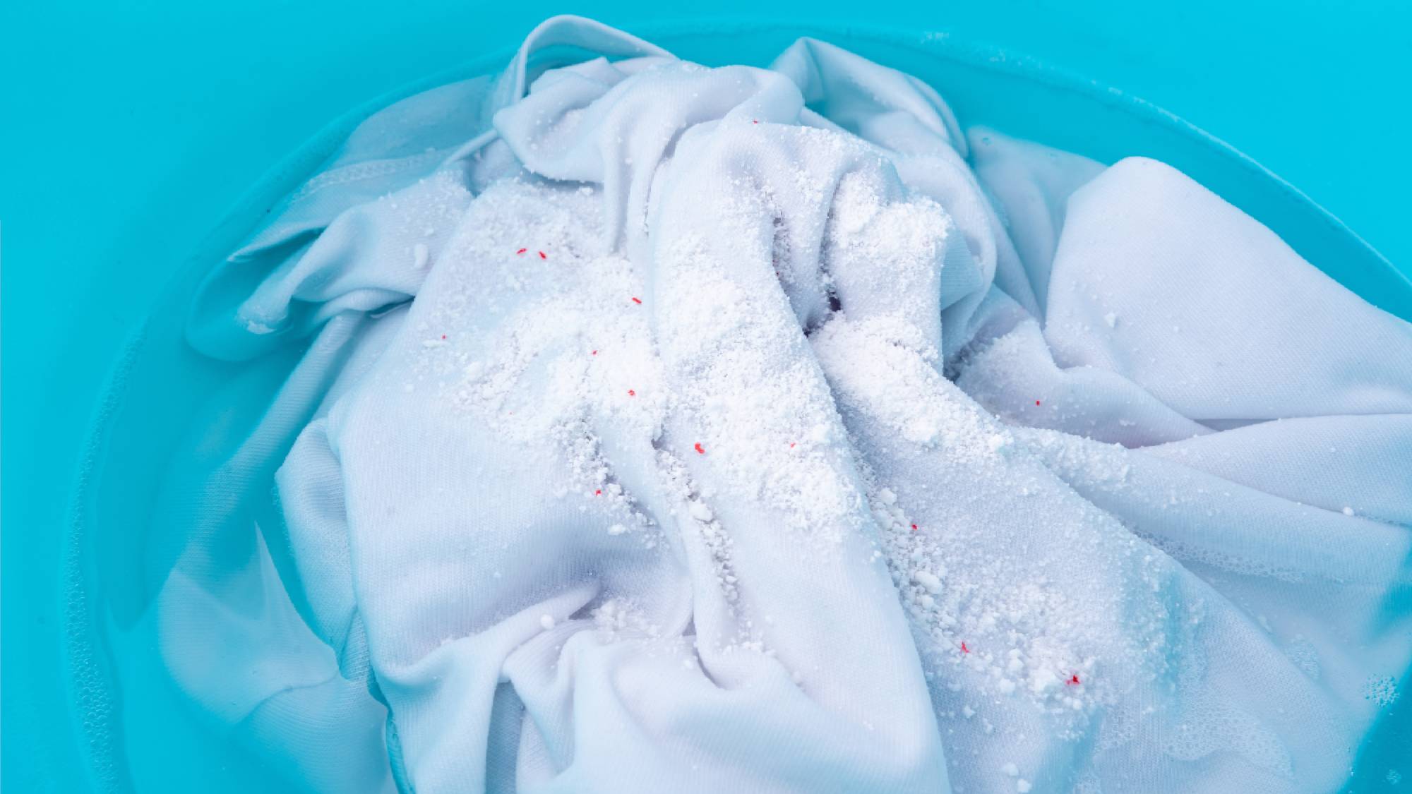Whites soaking in a blue washbasin with powdered oxygen bleach sprinkled on top to remove laundry stains.