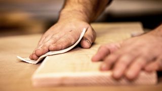 Close up of hands sanding a small plank of wood