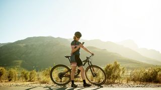 Photo of female cyclist stood next to a mountain bike while checking her phone