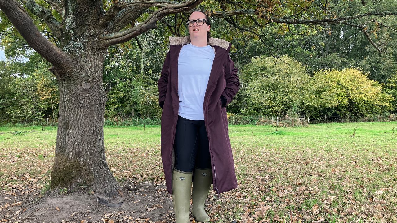 Lady wears LeMieux All Elements Robe standing by a tree unzipped, viewed from the front