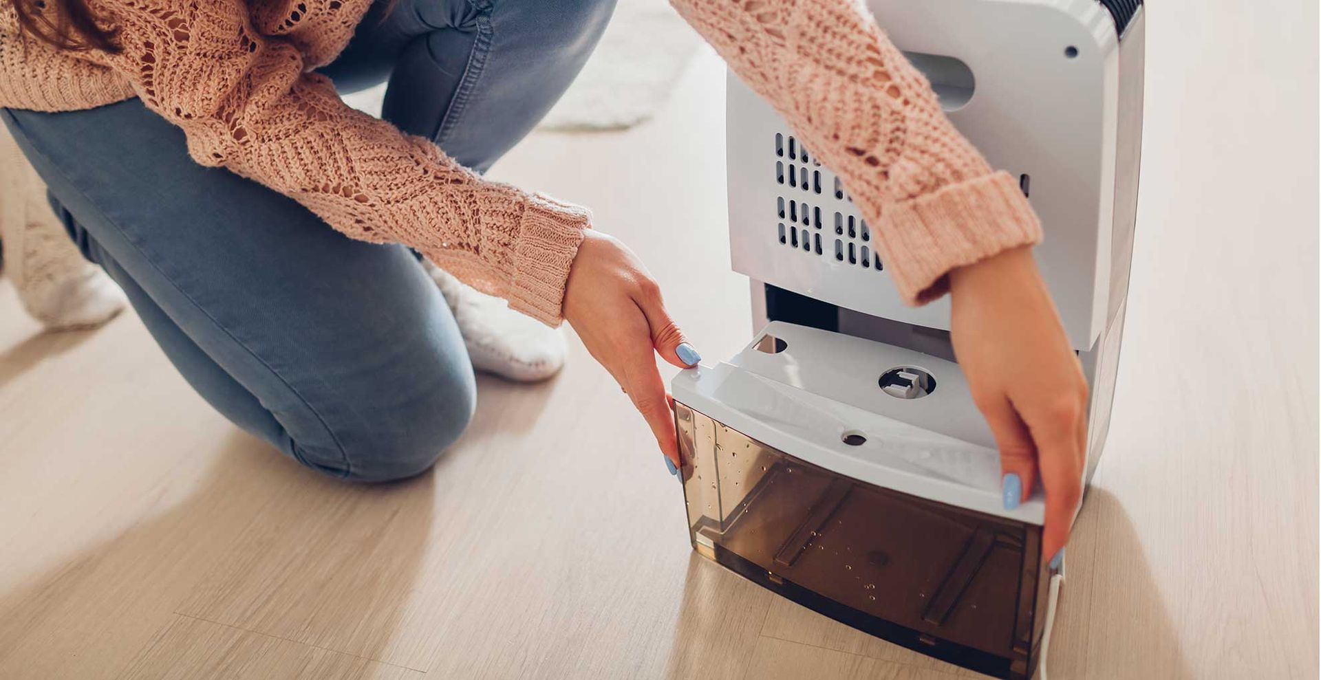 Person opening a dehumidifier to empty the tank demostrating what you need to know before buying a dehumidifier
