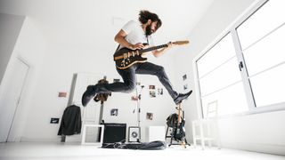 Man in white t-shirt and playing electric guitar leaps high in the air