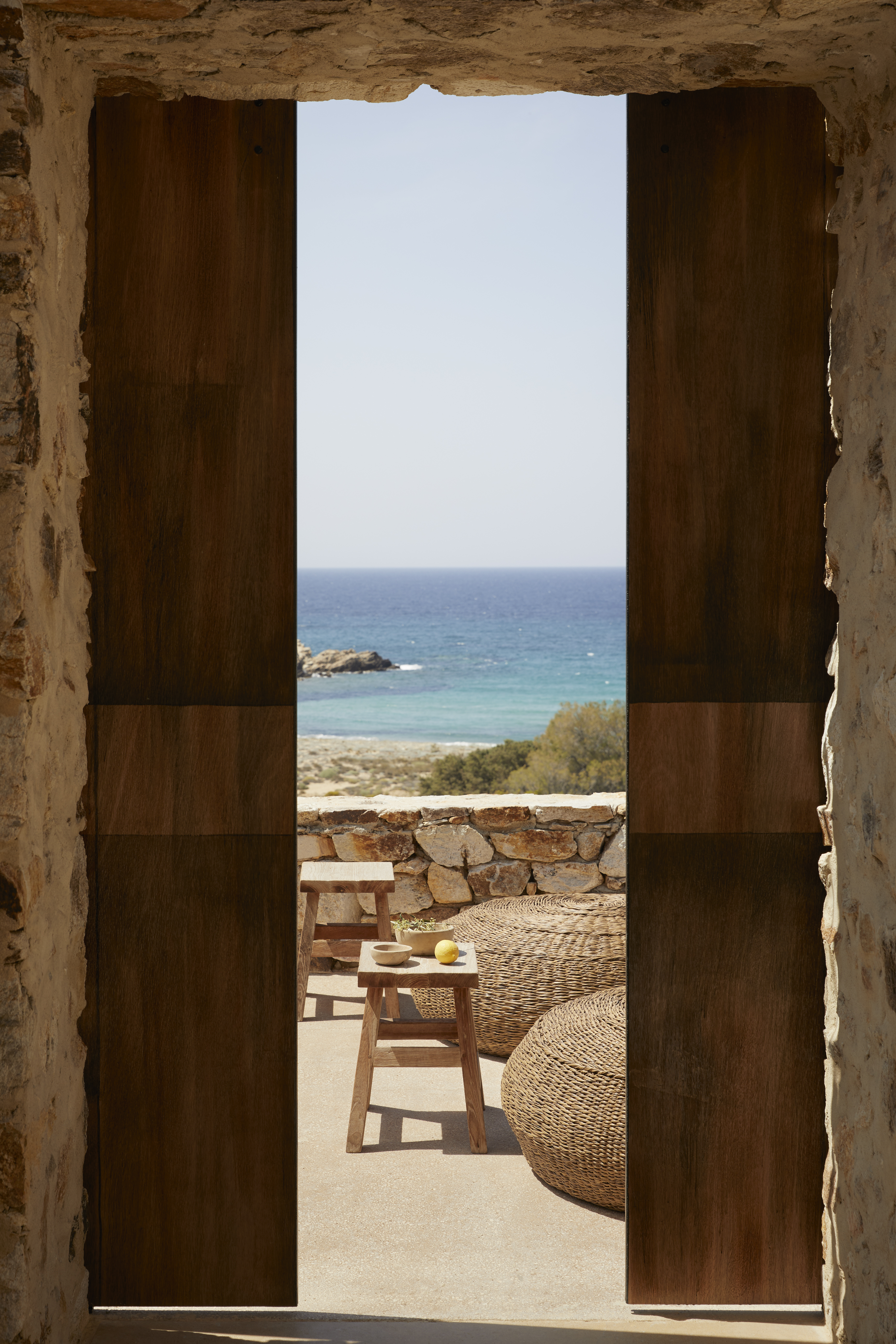 A tall wooden door, partially open onto a view of the Aegean sea