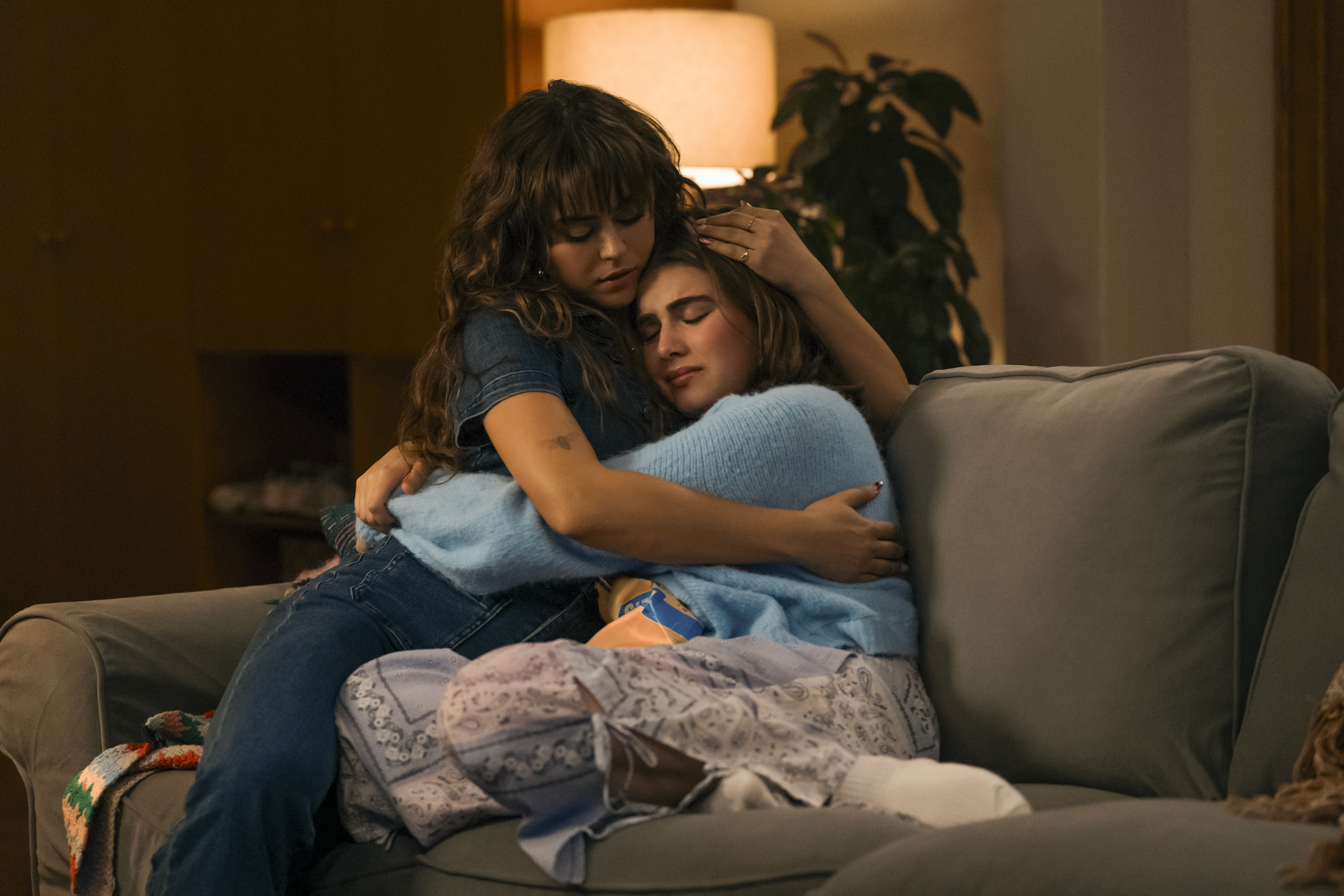 Allie Hayes (Mika Abdalla) and Hannah Wells (Ella Bright) hold each other while sitting on a couch, in OFF CAMPUS
