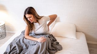 Woman waking up and sitting on her mattress holding her back in pain