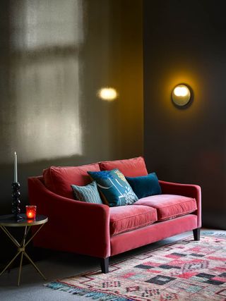 A red velvet sofa next to a round side table in an olive green living room
